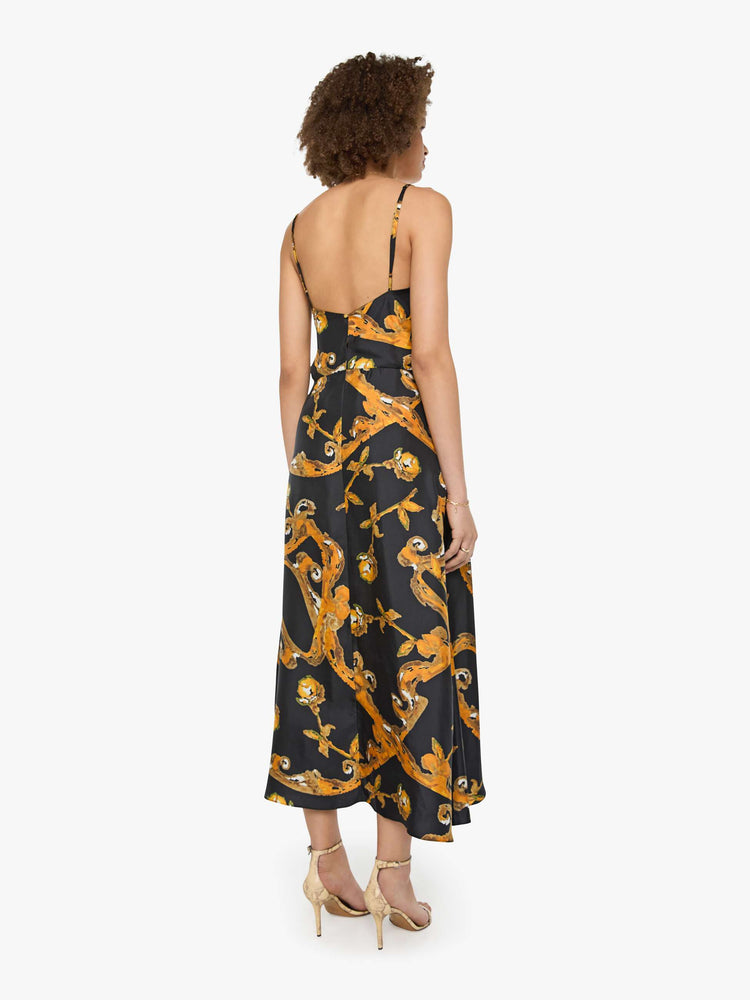Back  view of a woman in a black and gold prints with classic silhouettes, featuring a subtle V-neck, thin spaghetti straps, semi-fitted waist and a flowy ankle-length skirt.