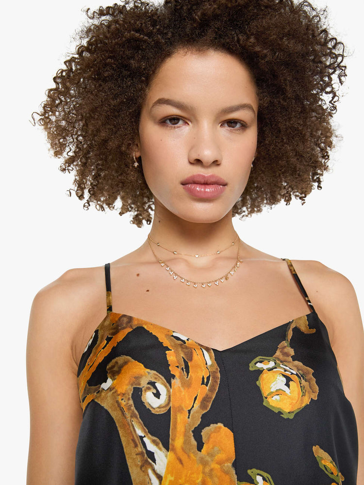 Close up  view of a woman in a black and gold prints with classic silhouettes, featuring a subtle V-neck, thin spaghetti straps, semi-fitted waist and a flowy ankle-length skirt.