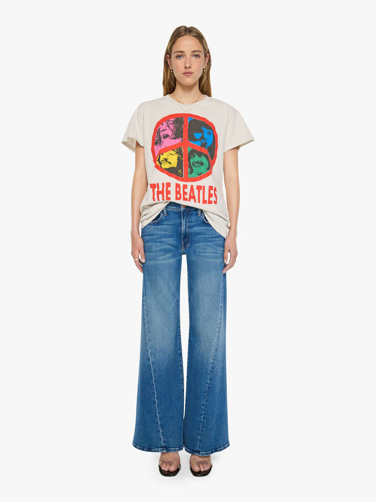 Full body view of a woman in vintage white tee pays homage to The Beatles with a red peace sign and graphic portraits on the front.