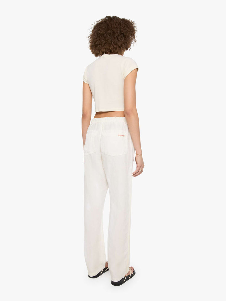 Back view of a woman in white with a hand-drawn koi fish screen-printed on the left side pocket, the pants have oversized patch pockets, an extra-long inseam that puddles at the hem and a woven belt that ties.
