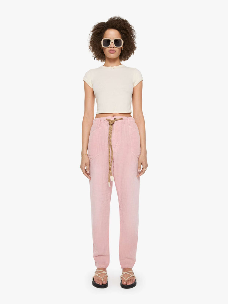 Front view of a woman in pink pants have oversized patch pockets, an extra-long inseam that puddles at the hem and a woven belt that ties.