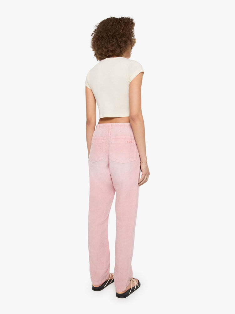Back view of a woman in pink pants have oversized patch pockets, an extra-long inseam that puddles at the hem and a woven belt that ties.