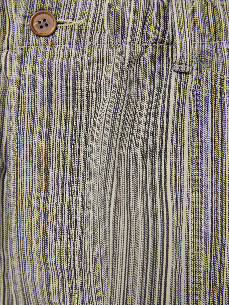Swatch view of a woman in faded grey with vertical stripes pants with a mid rise with oversized pockets, an extra-long inseam that puddles at the hem and a colorful woven belt that ties.