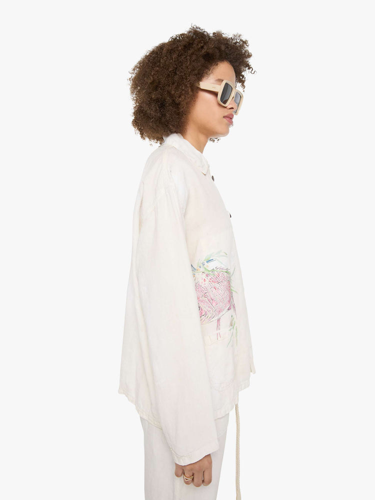 Side view of a woman in a white jacket with a hand-drawn koi fish screen-printed on the right chest, the button-up jacket has patch pockets, dropped shoulders and a relaxed fit.
