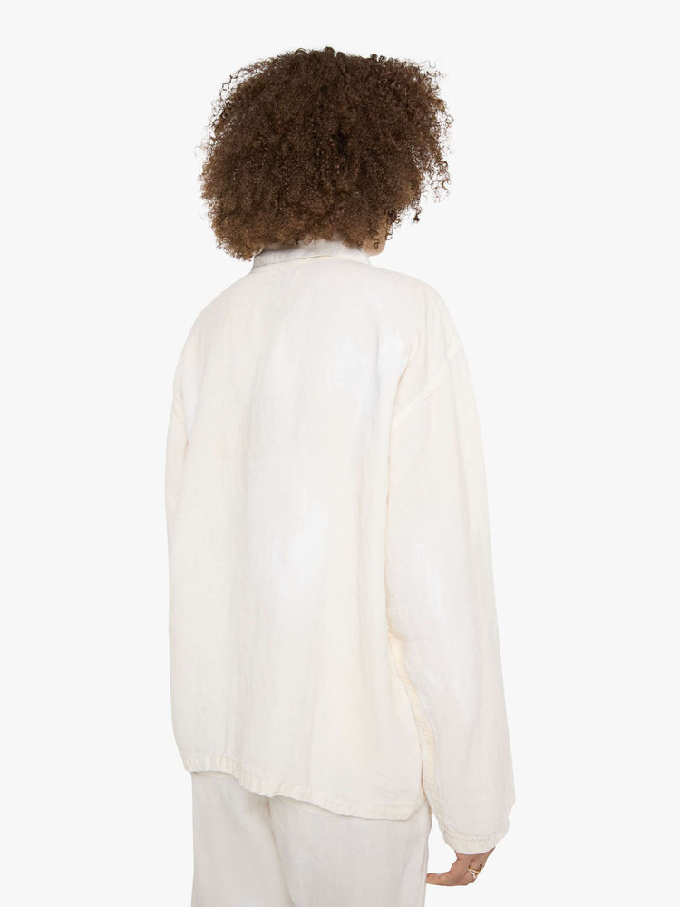 Back view of a woman in a white jacket with a hand-drawn koi fish screen-printed on the right chest, the button-up jacket has patch pockets, dropped shoulders and a relaxed fit.