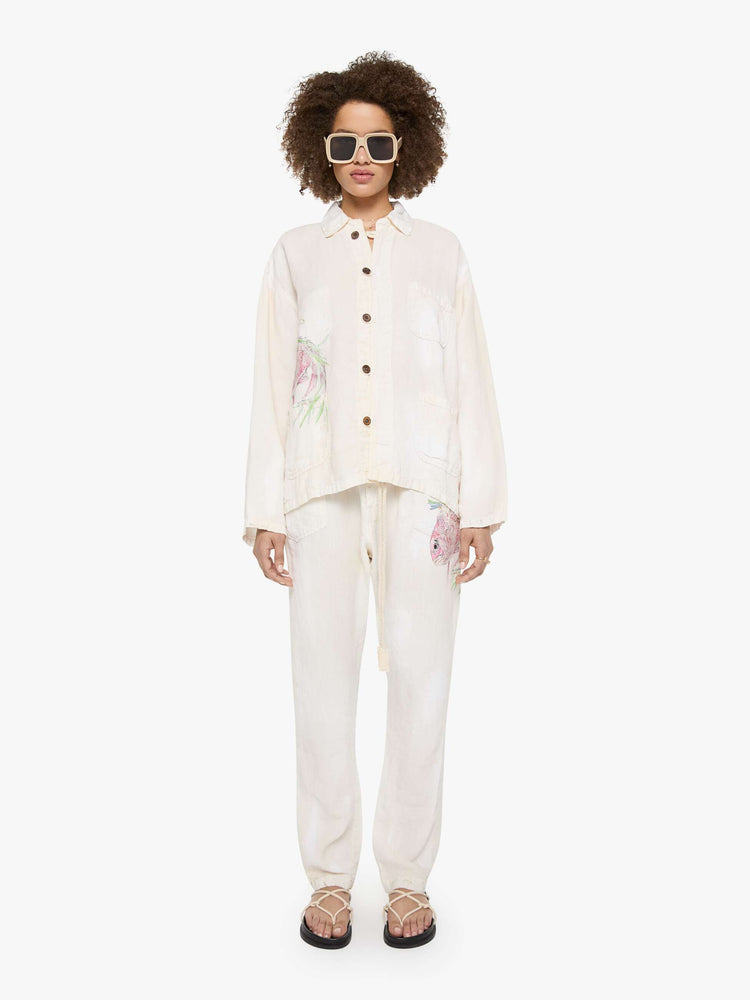 Full body view of a woman in a white jacket with a hand-drawn koi fish screen-printed on the right chest, the button-up jacket has patch pockets, dropped shoulders and a relaxed fit.