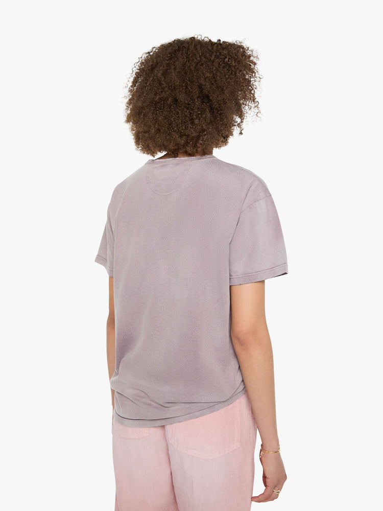 Back view of a woman in a dusty orchid tee with a scene from Menorca, Spain, in faded blue.