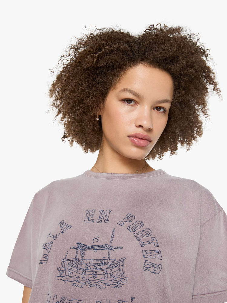 Close up view of a woman in a dusty orchid tee with a scene from Menorca, Spain, in faded blue.