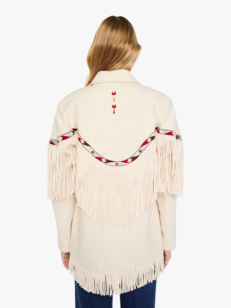Back view of a woman in a cream jacket with decorative embroidery, patch pockets, fringe at the chest and hem and a boxy fit.