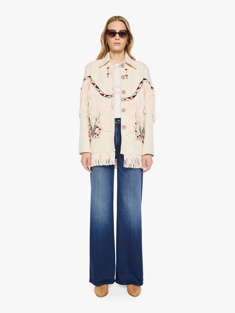 Front view of a woman in a cream jacket with decorative embroidery, patch pockets, fringe at the chest and hem and a boxy fit.