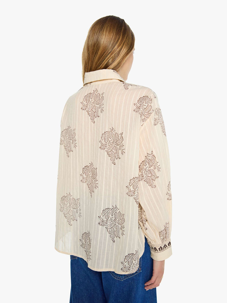 Back view of a woman in cream button up with an oversized floral print, and features a stacked collar, long balloon sleeves and ruffles throughout for a loose, flowy fit.