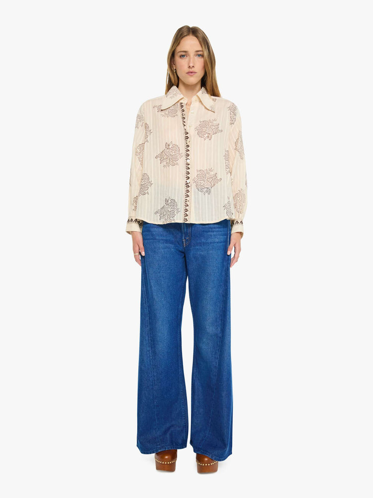 Full body view of a woman in cream button up with an oversized floral print, and features a stacked collar, long balloon sleeves and ruffles throughout for a loose, flowy fit.
