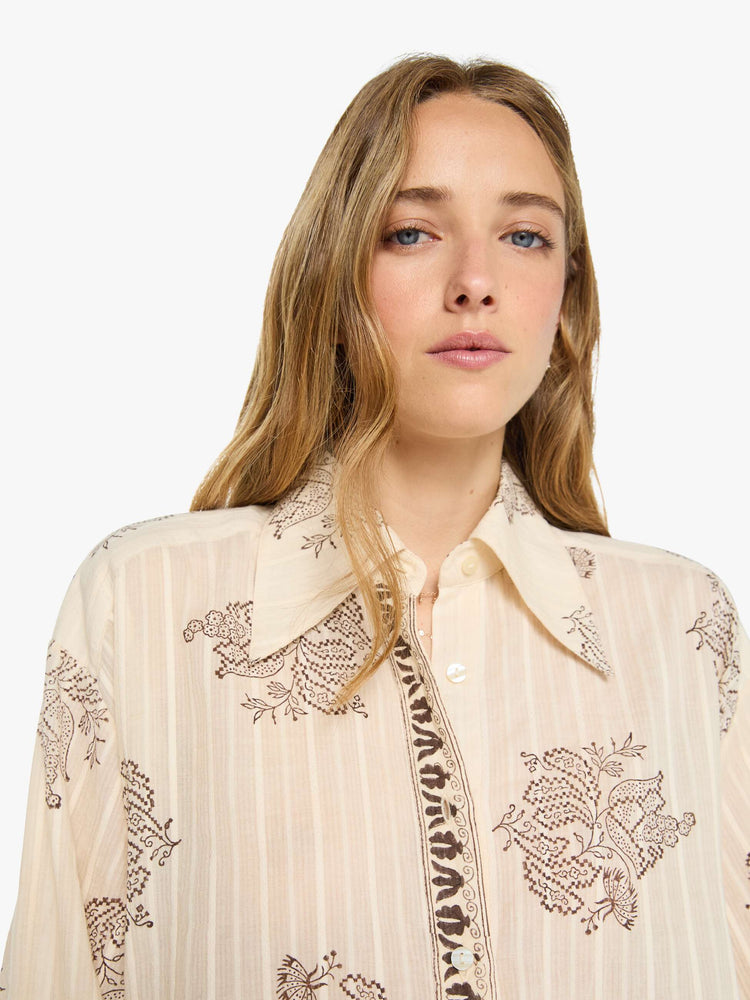 Close up view of a woman in cream button up with an oversized floral print, and features a stacked collar, long balloon sleeves and ruffles throughout for a loose, flowy fit.