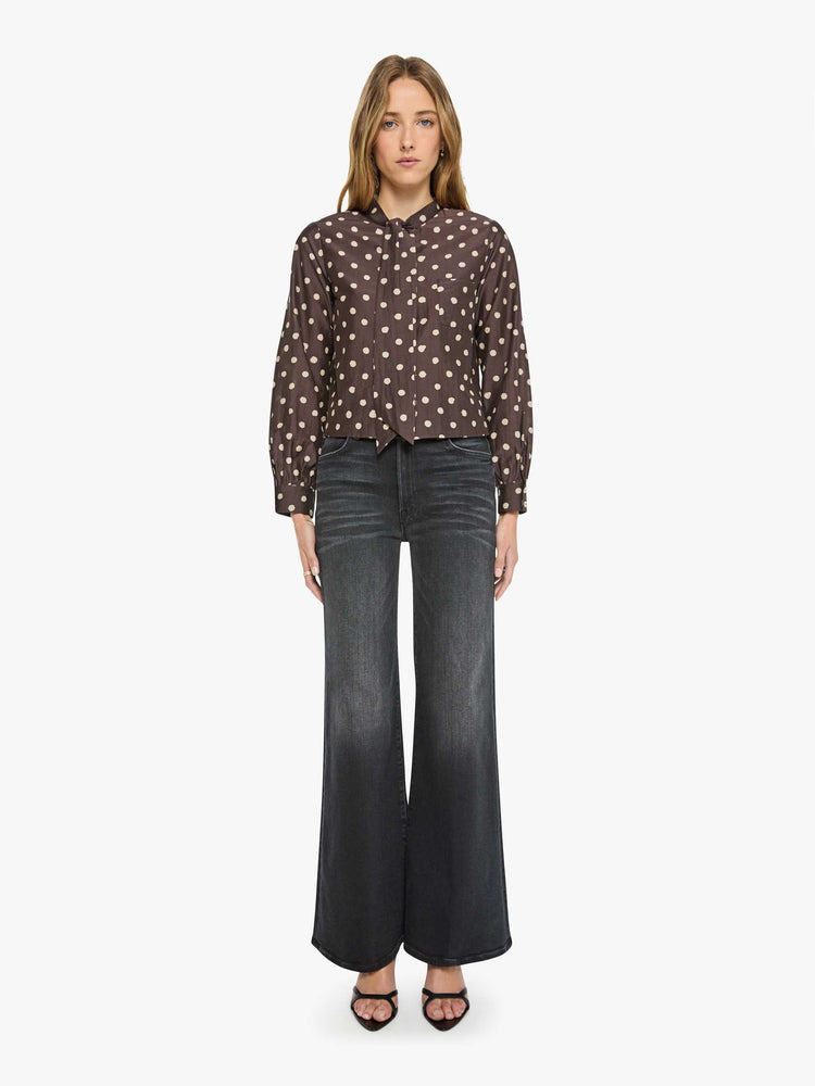 Full body view of a woman in a mahogany with cream polka dots shirt with a collared neck that ties, long balloon sleeves and a cropped fit.