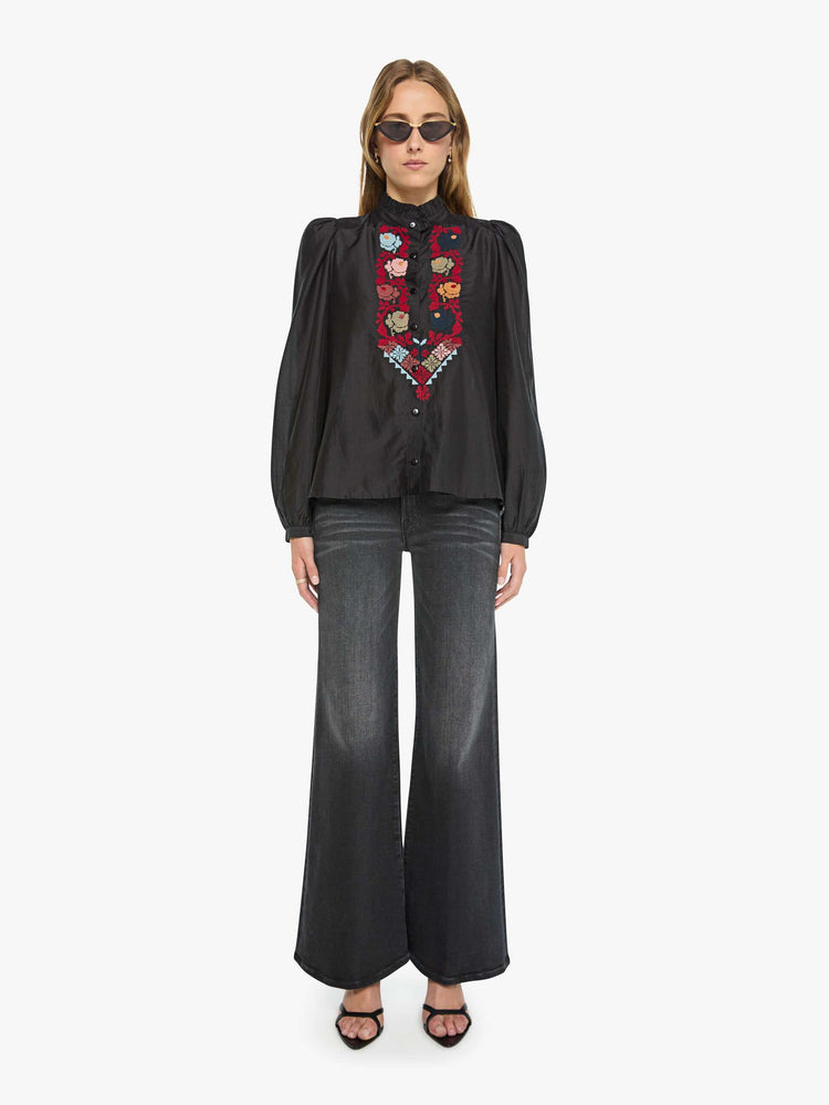 Full body view of a woman in a black with a floral-detailed panel in dark red down the front top and features a stacked collar, puff shoulders, long balloon sleeves and a loose fit.