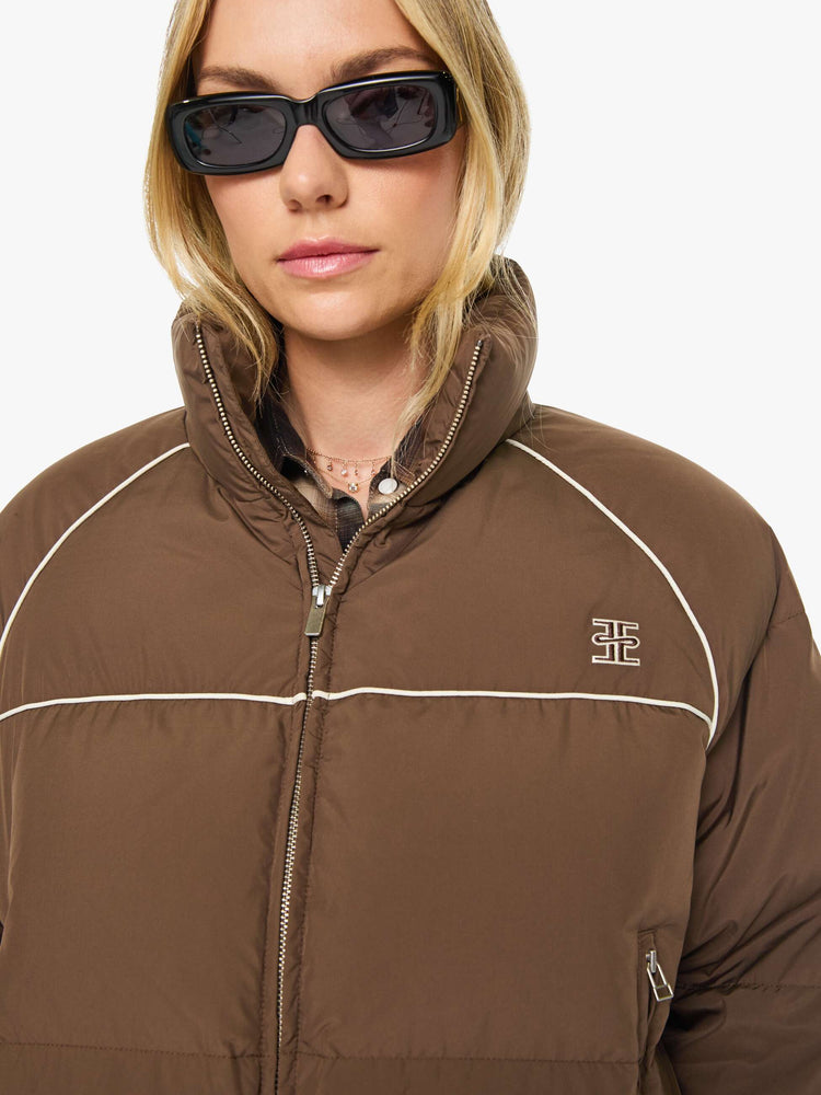 Close up view of a woman in brown with cream piping jacket has a high neck, front zip pockets, elastic hems and a cropped fit.