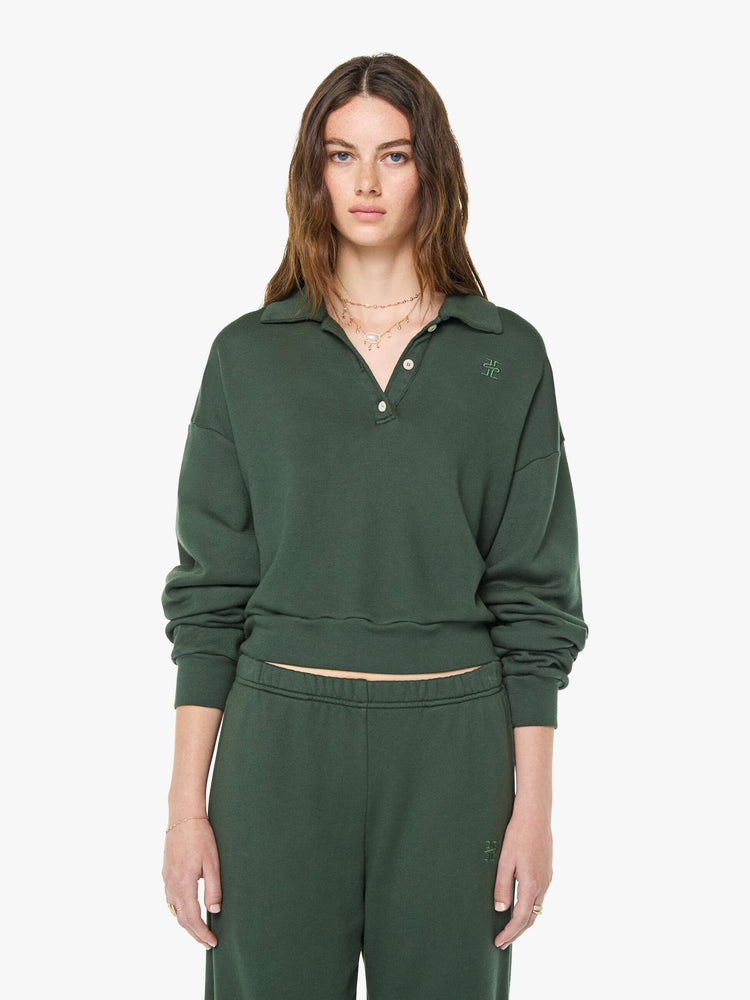 Front view of a woman in a forest green polo sweatshirt with a buttoned V-neck, drop shoulders, long sleeves and a cropped fit.