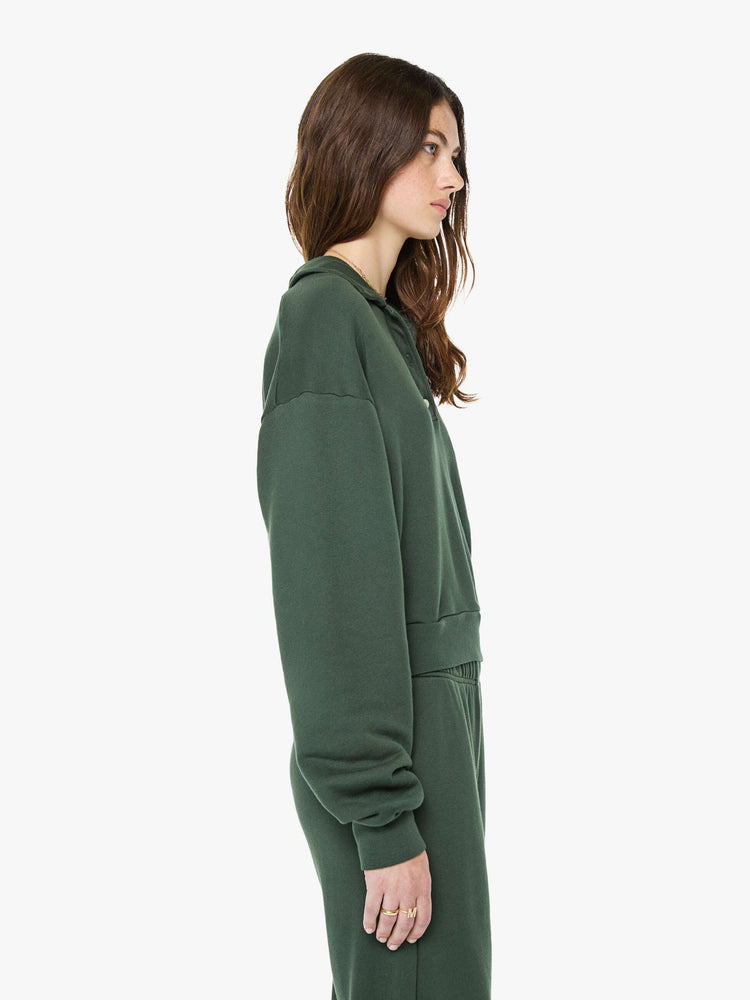 Side view of a woman in a forest green polo sweatshirt with a buttoned V-neck, drop shoulders, long sleeves and a cropped fit.