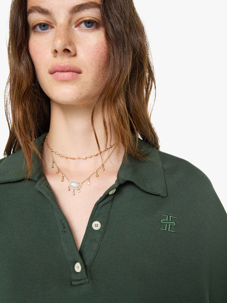Close up view of a woman in a forest green polo sweatshirt with a buttoned V-neck, drop shoulders, long sleeves and a cropped fit.