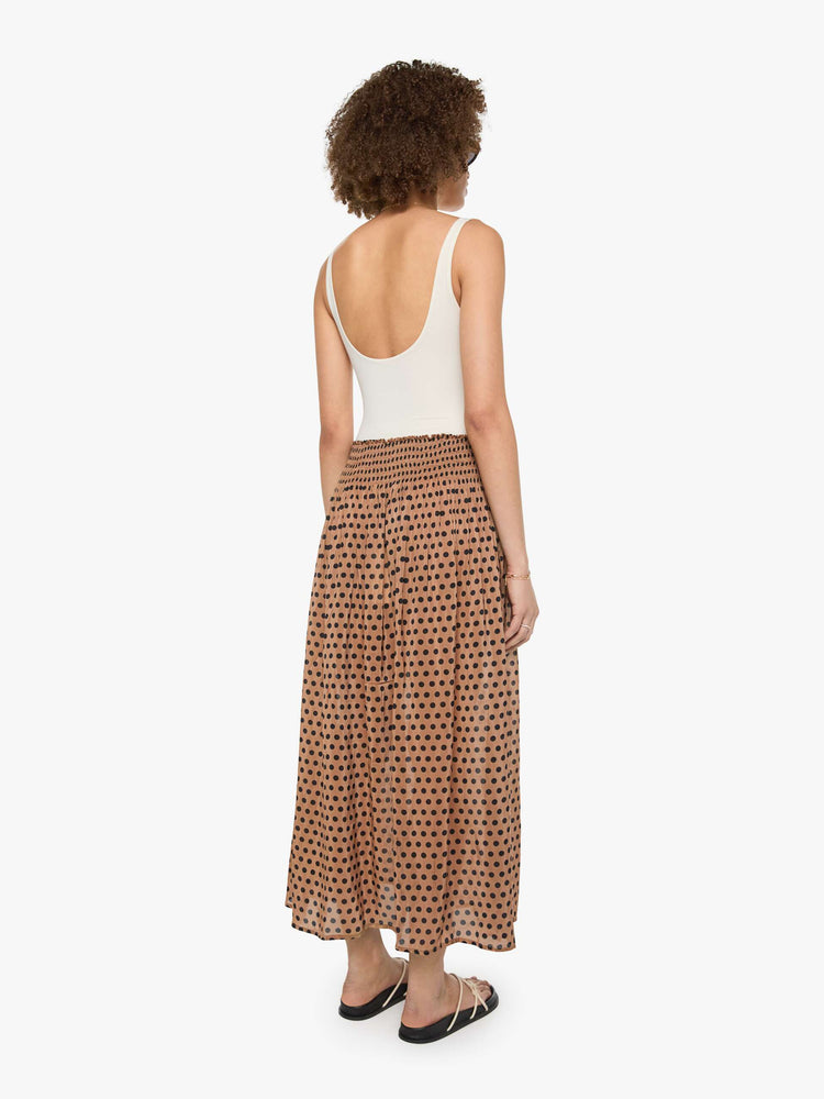 Back view of a woman in a tan with black polka dots maxi skirt has a smocked waistband and a loose, flowy fit.