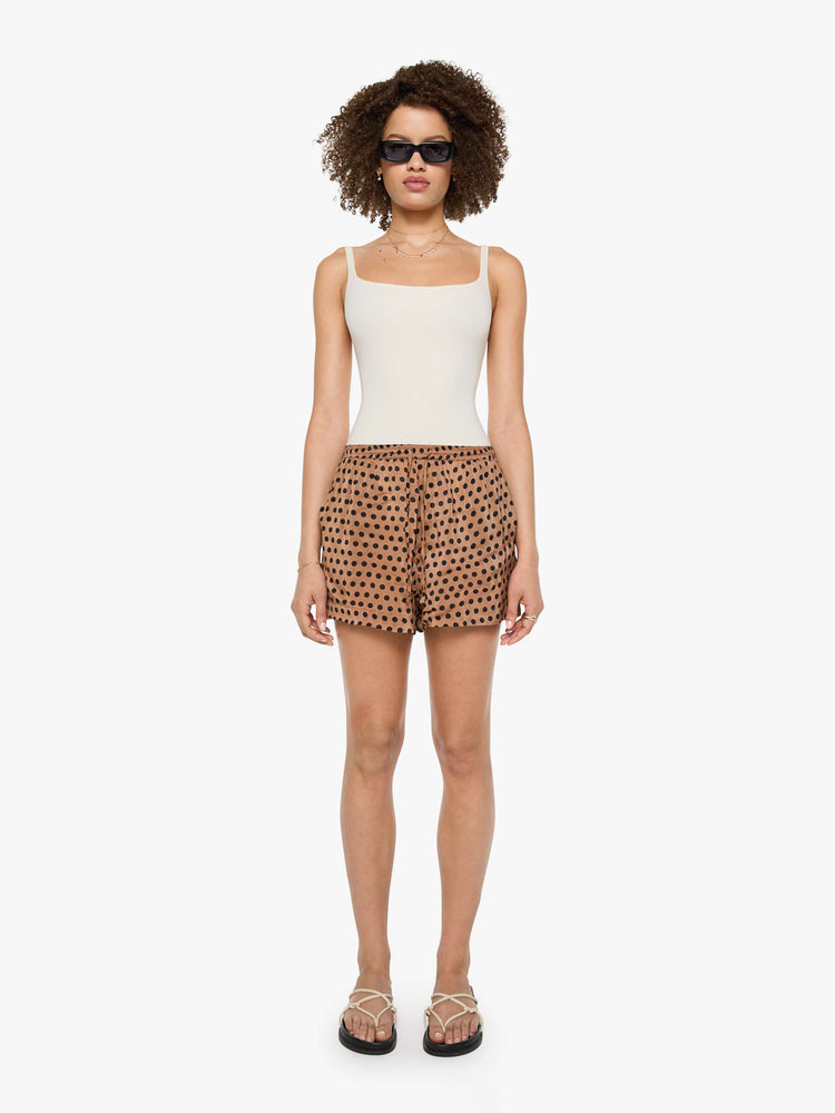 Front view of a woman in tan and black polk dots shorts with an elastic high waist, side slit pockets, a slightly curved hem and a loose, flowy fit.