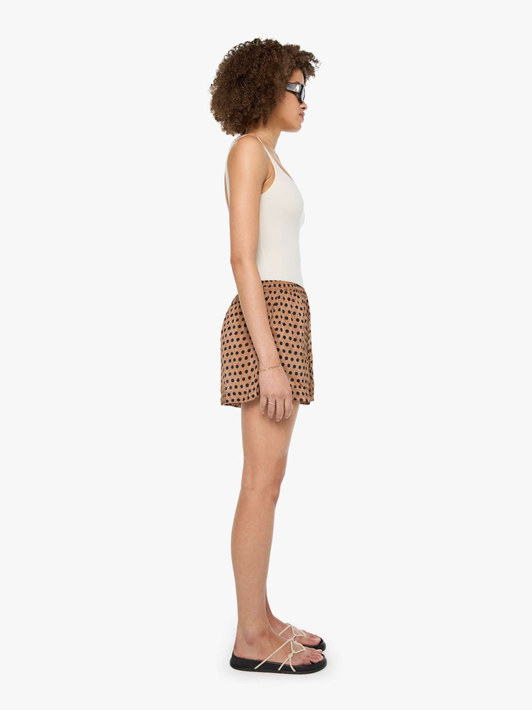 Side view of a woman in tan and black polk dots shorts with an elastic high waist, side slit pockets, a slightly curved hem and a loose, flowy fit.