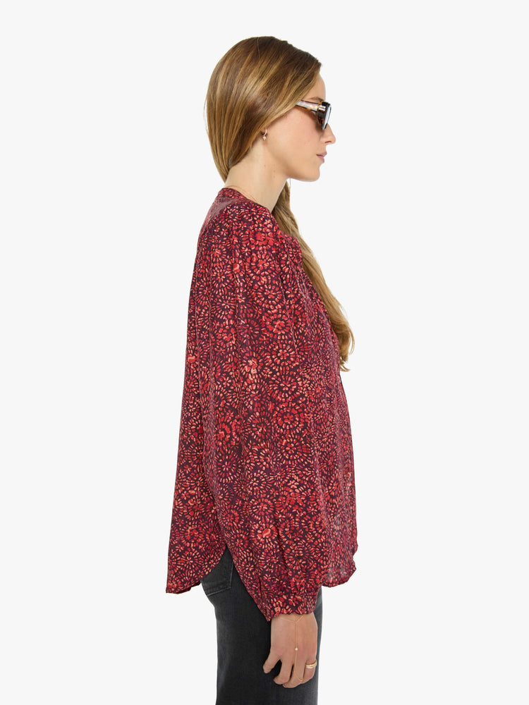 Side view of a woman deep red shirt with a floral print, and features a crewneck, long balloon sleeves and ruffles throughout for a flowy fit.