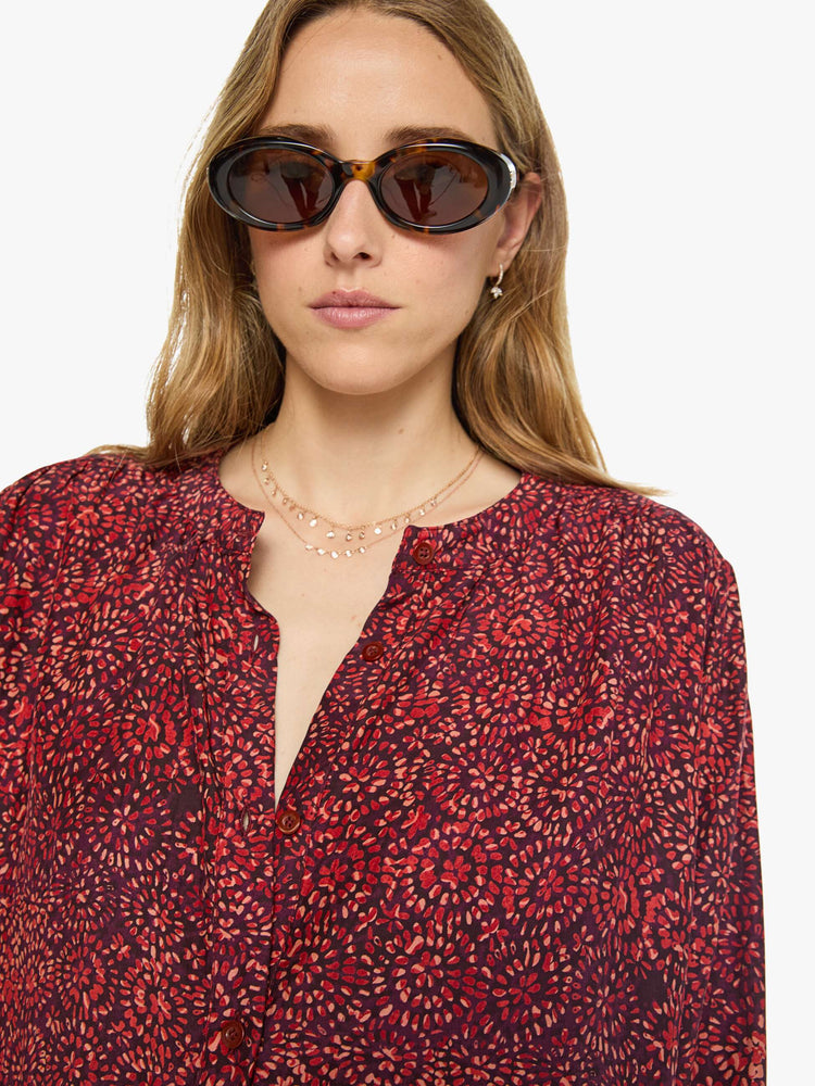 Close up view of a woman deep red shirt with a floral print, and features a crewneck, long balloon sleeves and ruffles throughout for a flowy fit.