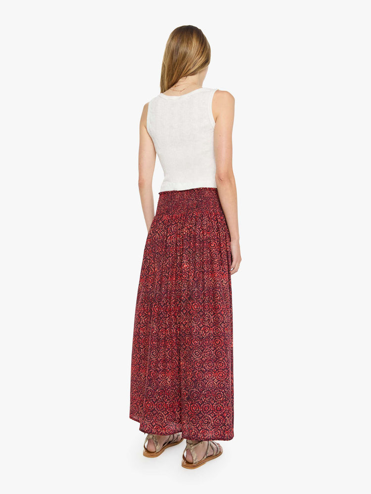 Back view of a woman in a  deep red with a floral print skirt has a smocked waistband and a loose, flowy fit. 