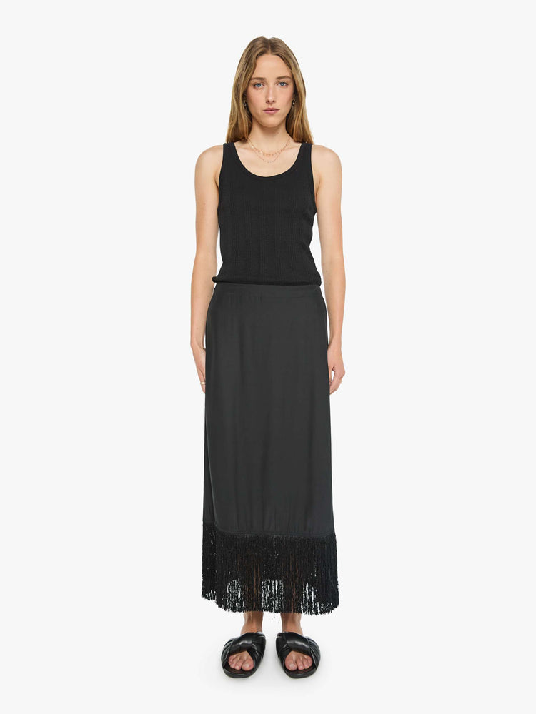Front view of a woman in black skirt has a high rise, fringed, calf-length hem and a loose, flowy fit.