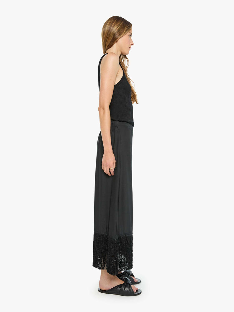Side view of a woman in black skirt has a high rise, fringed, calf-length hem and a loose, flowy fit.