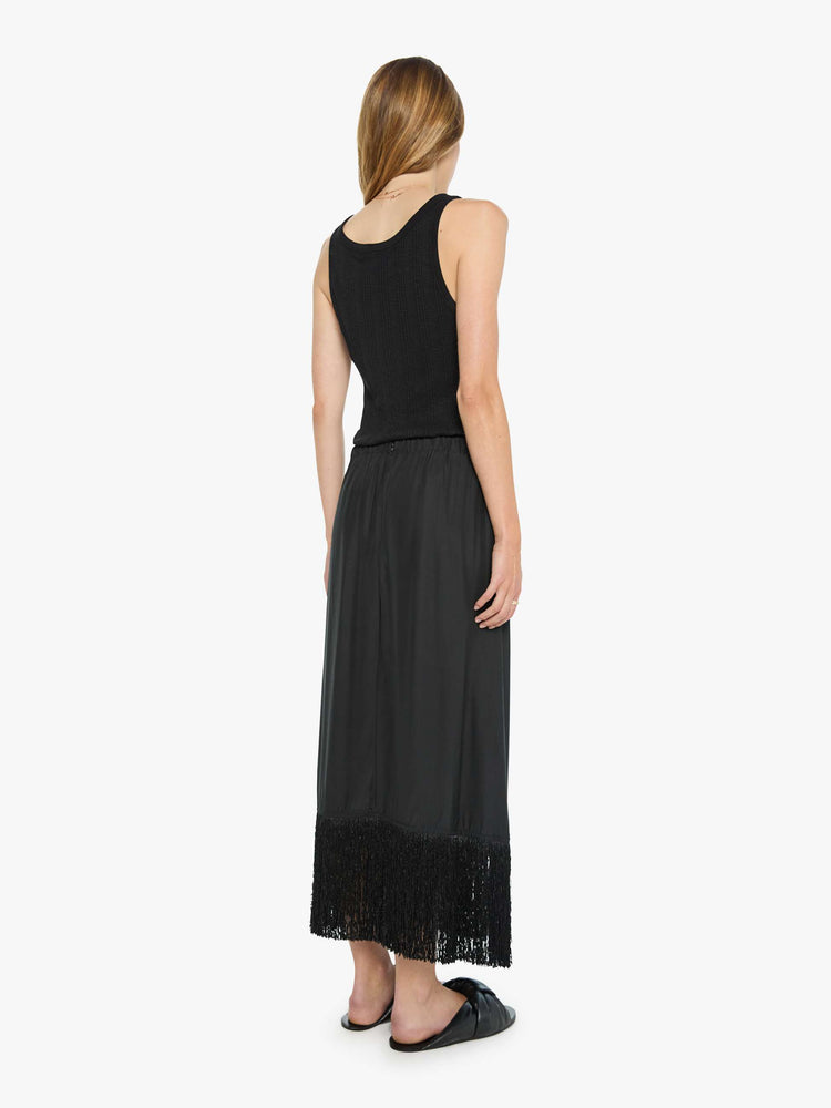 Back view of a woman in black skirt has a high rise, fringed, calf-length hem and a loose, flowy fit.