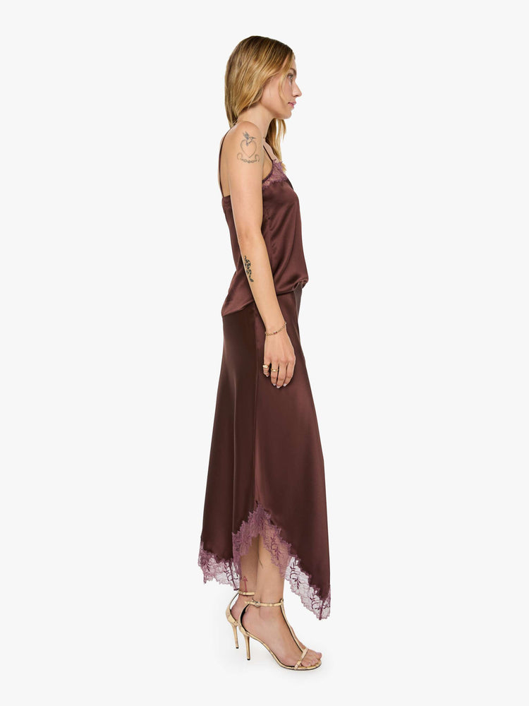 Side view of a woman in a silk in a chocolate brown with lace trim, the maxi skirt is designed with a flowy fit and an uneven, ankle-grazing hem.