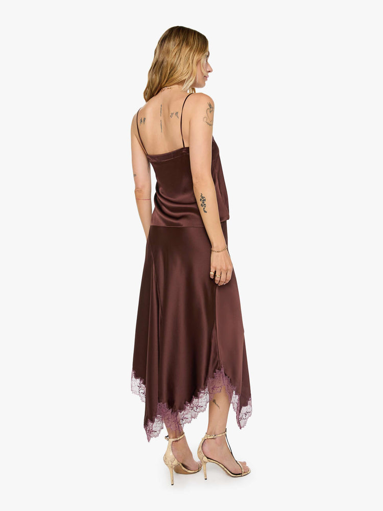 Back view of a woman in a silk in a chocolate brown with lace trim, the maxi skirt is designed with a flowy fit and an uneven, ankle-grazing hem.
