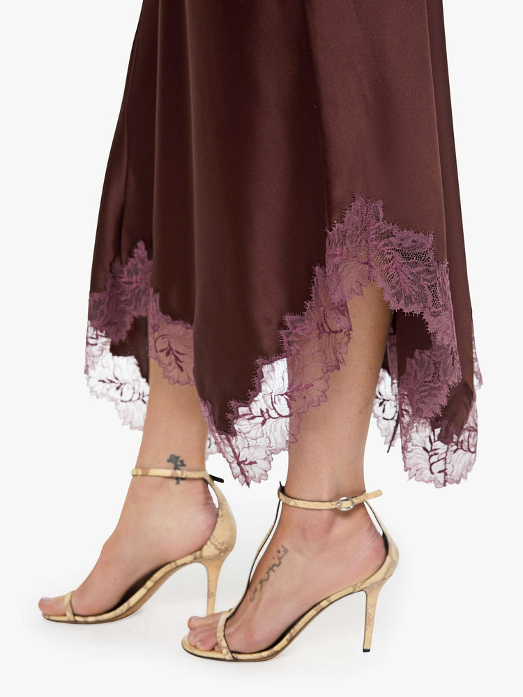 Hem close up view of a woman in a silk in a chocolate brown with lace trim, the maxi skirt is designed with a flowy fit and an uneven, ankle-grazing hem.