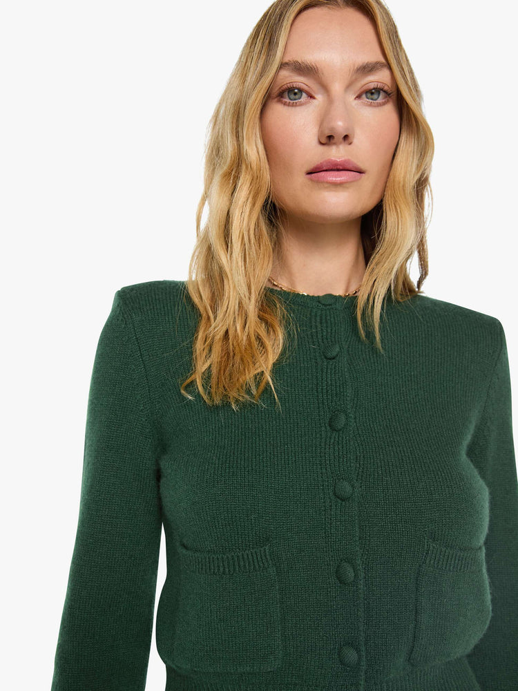 Close up view of a woman in green cardigan is designed with a crewneck, long sleeves, ribbed hems and a cropped fit.
