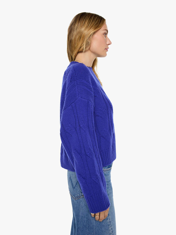 Side view of a woman in a cobalt blue with a cable knit pattern sweater with a crewneck, long sleeves, ribbed hems and a slightly oversized fit.