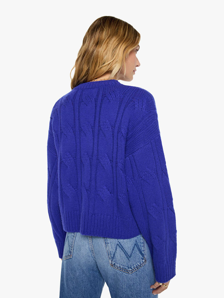 Back view of a woman in a cobalt blue with a cable knit pattern sweater with a crewneck, long sleeves, ribbed hems and a slightly oversized fit.