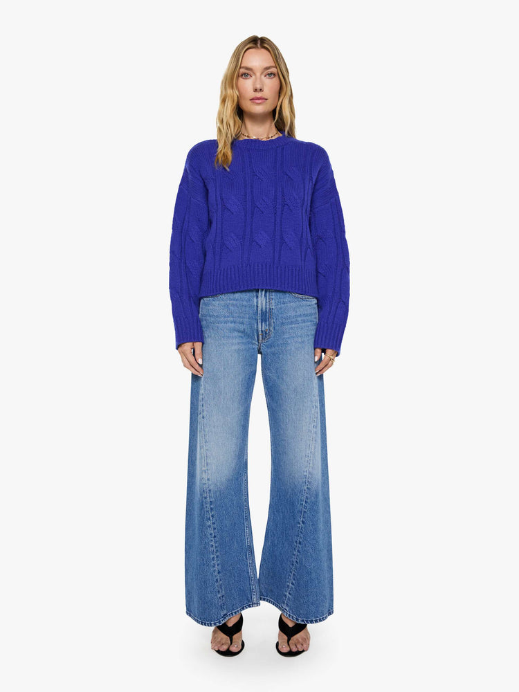 Full body view of a woman in a cobalt blue with a cable knit pattern sweater with a crewneck, long sleeves, ribbed hems and a slightly oversized fit.