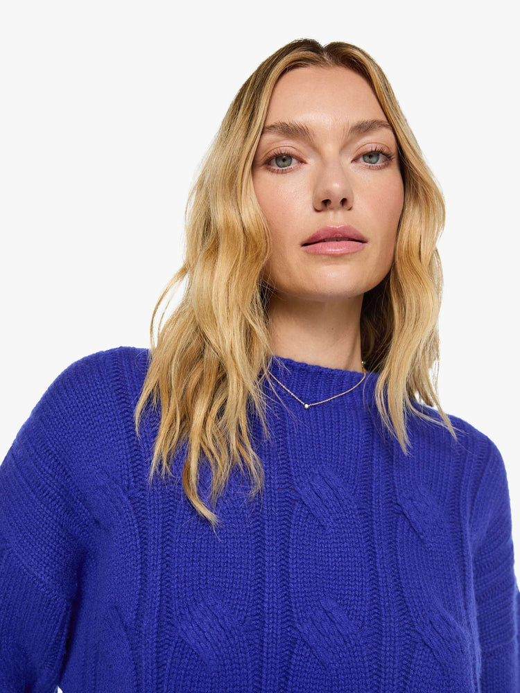 Close up view of a woman in a cobalt blue with a cable knit pattern sweater with a crewneck, long sleeves, ribbed hems and a slightly oversized fit.