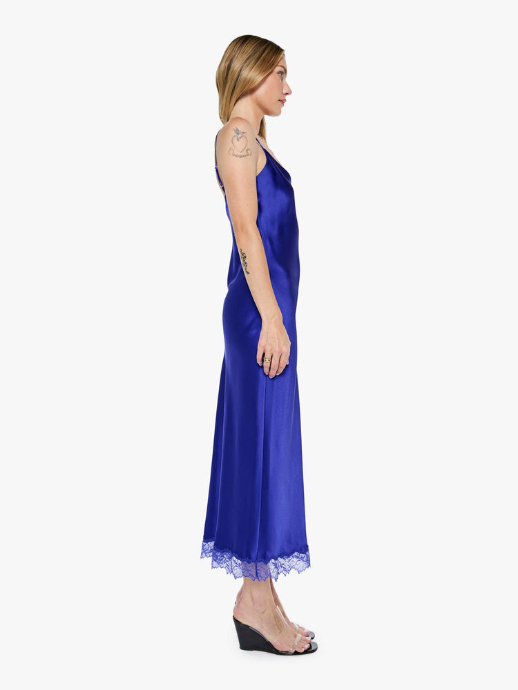 Side view of a woman in a slip cobalt blue dress is designed with thin spaghetti straps, a V-neck, lace trim, an ankle-length hem and a loose, flowy fit.