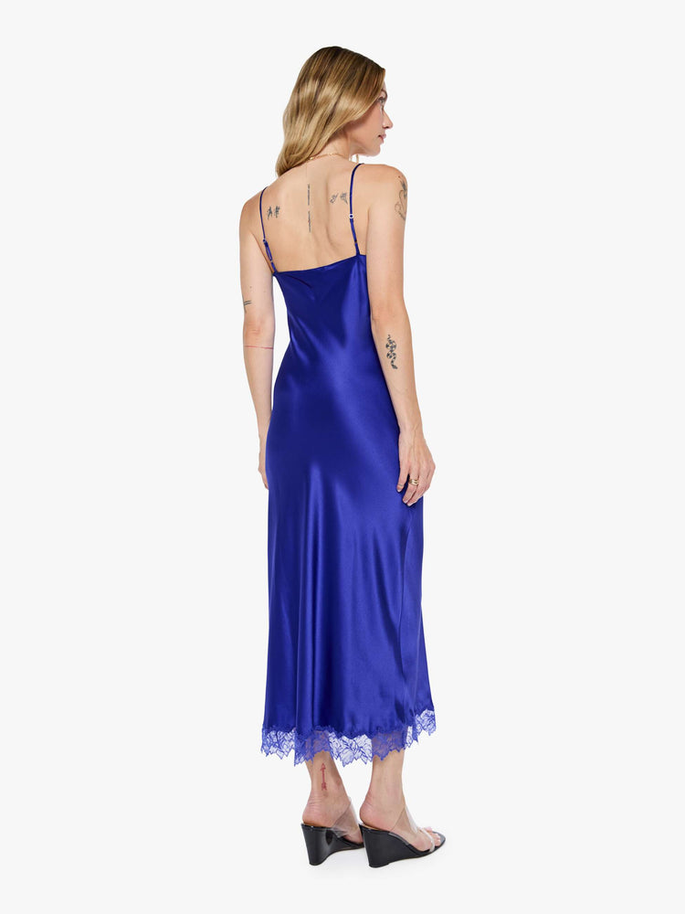 Back view of a woman in a slip cobalt blue dress is designed with thin spaghetti straps, a V-neck, lace trim, an ankle-length hem and a loose, flowy fit.