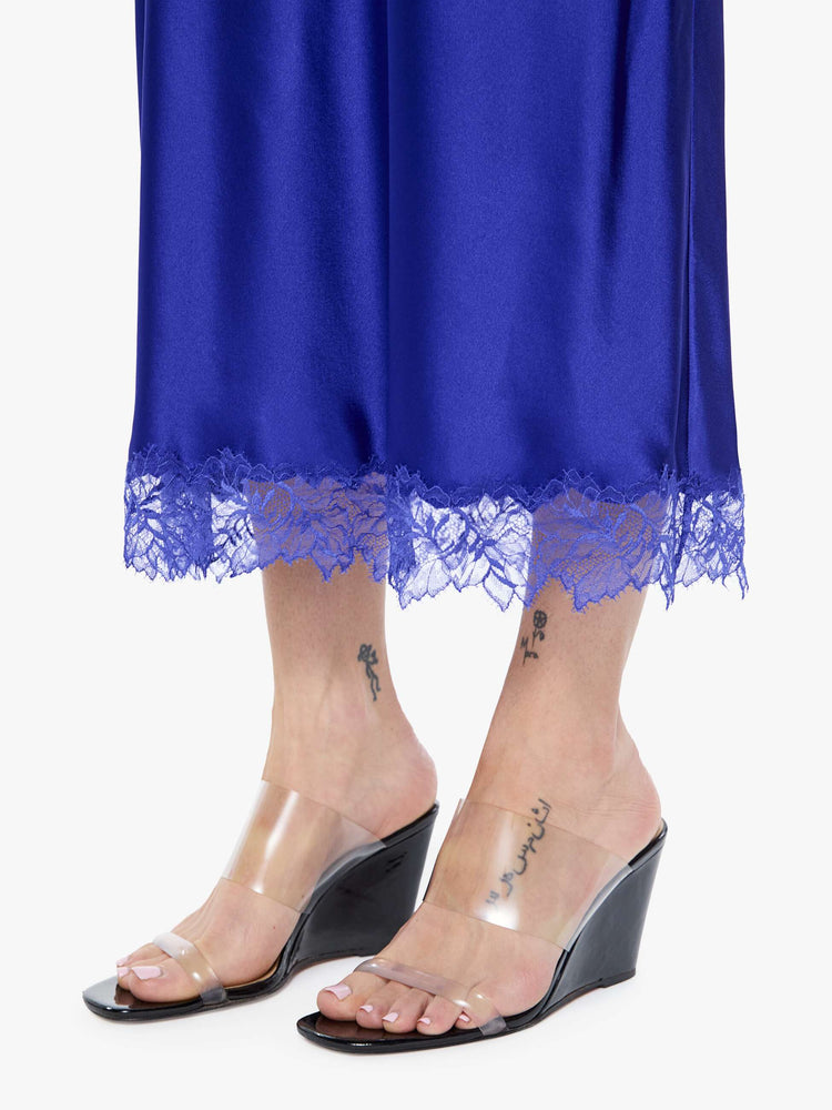 Hem close up view of a woman in a slip cobalt blue dress is designed with thin spaghetti straps, a V-neck, lace trim, an ankle-length hem and a loose, flowy fit.