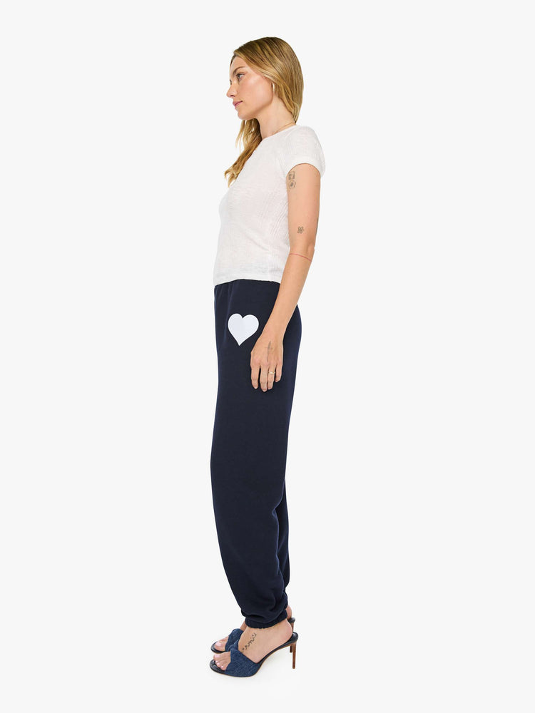 Side view of a woman in a navy with white heart on the hip sweatpants have an elastic waist and cuffs for a loose, comfortable fit.