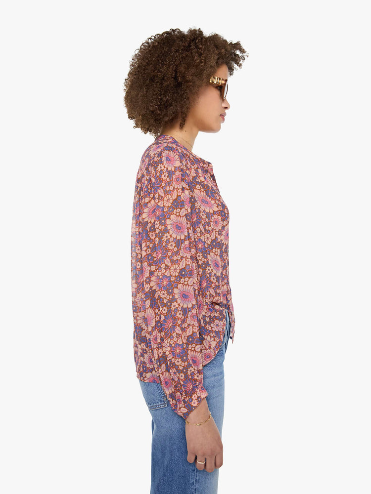 Side view of a woman in warm-toned floral print button up top with a V-neck, long balloon sleeves and curved hem with a light and airy fit.