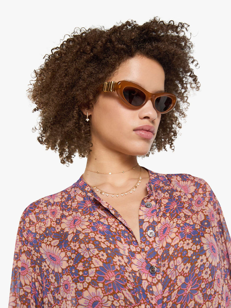 Close up view of a woman in warm-toned floral print button up top with a V-neck, long balloon sleeves and curved hem with a light and airy fit.