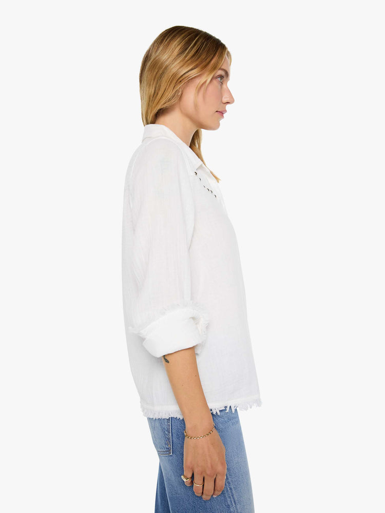 Side view of a woman in a white with a V-neck top features studded details across the chest and fringe at the hem.