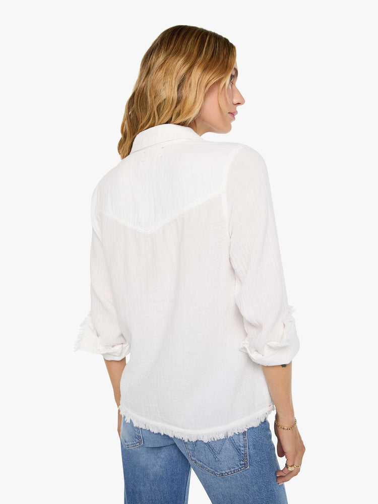Back view of a woman in a white with a V-neck top features studded details across the chest and fringe at the hem.