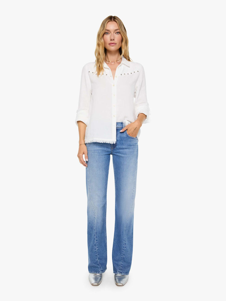 Full body view of a woman in a white with a V-neck top features studded details across the chest and fringe at the hem.