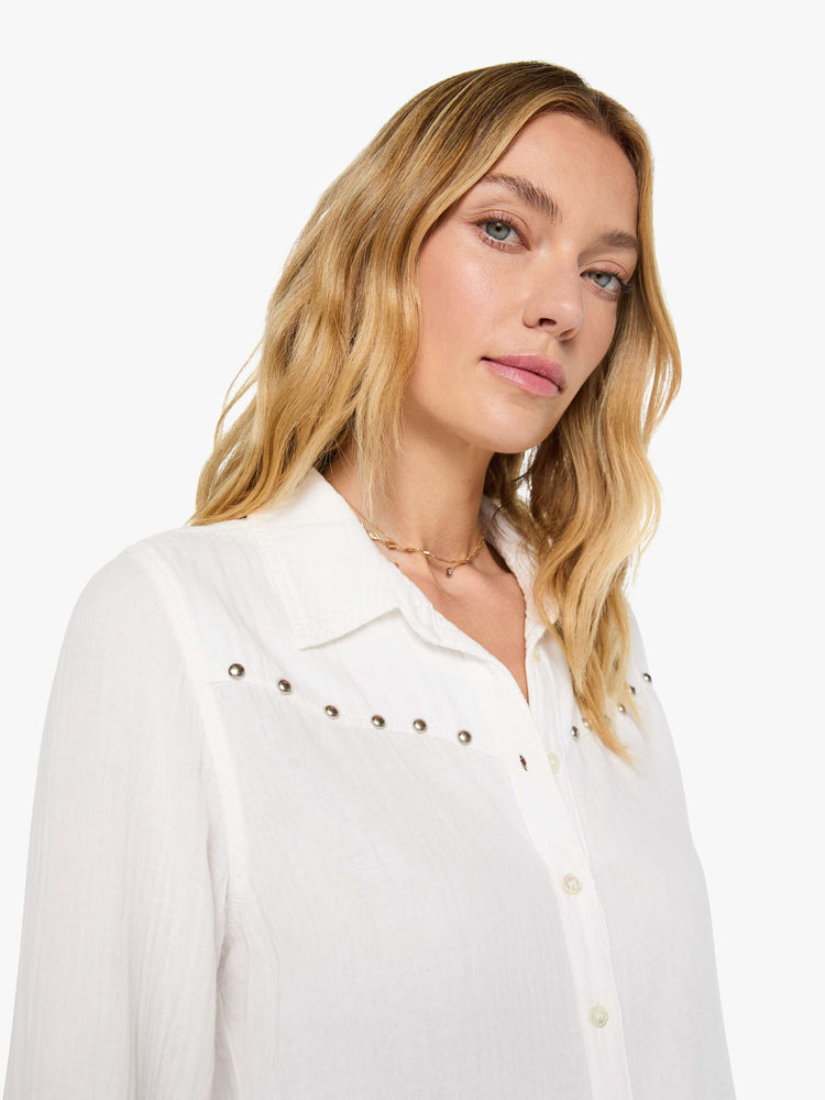 Clos up view of a woman in a white with a V-neck top features studded details across the chest and fringe at the hem.